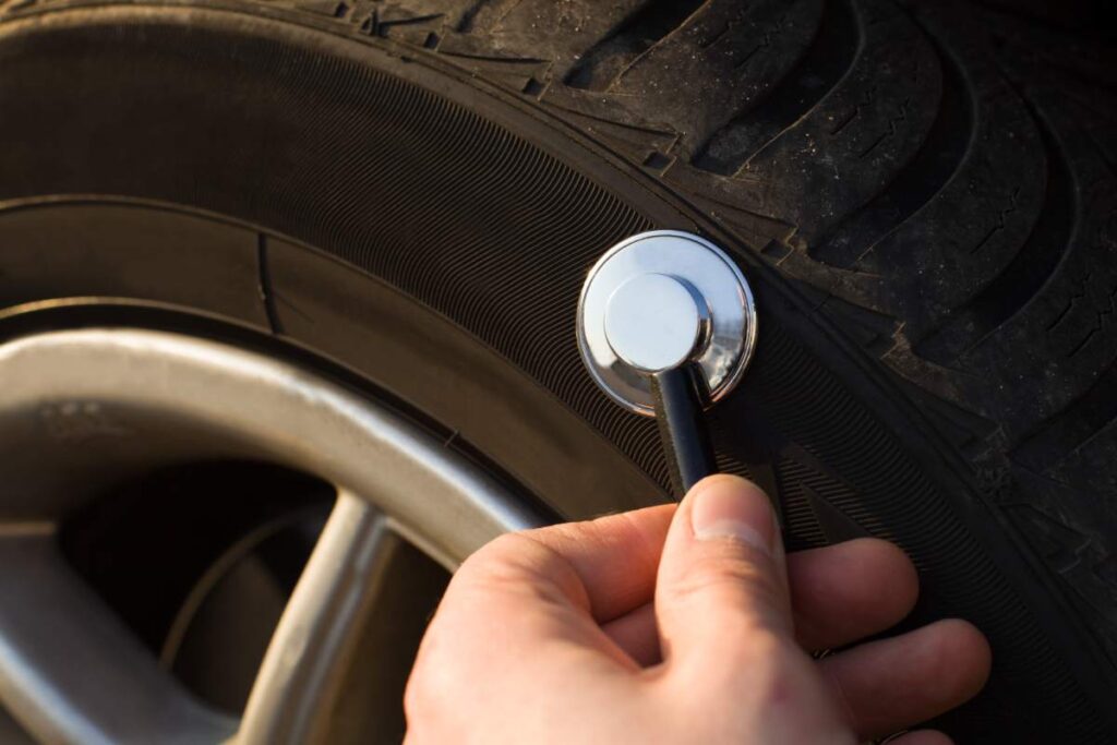 Close-up of someone's hand using a stethoscope to check a car tire, showcasing vehicle check up.