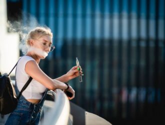 Young woman outdoor vaping e-cigarette on modern city buildings background