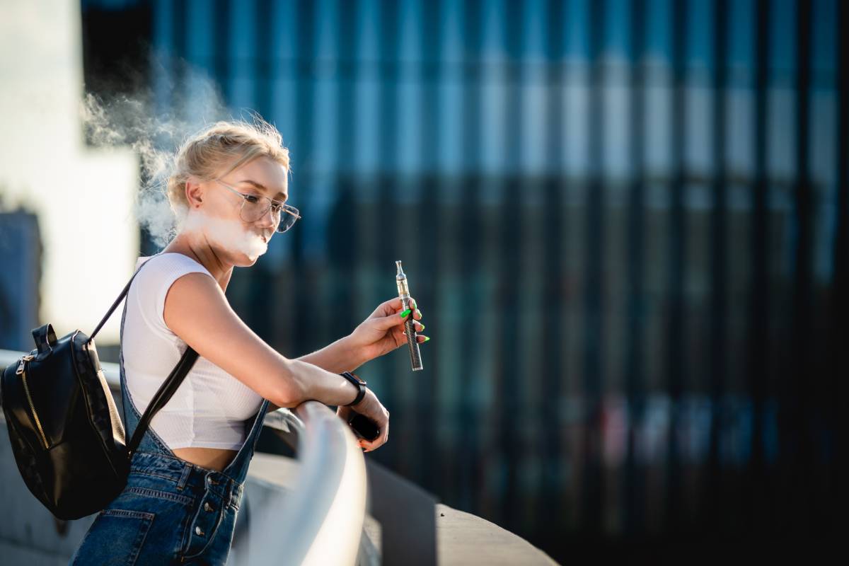 Young woman outdoor vaping e-cigarette on modern city buildings background
