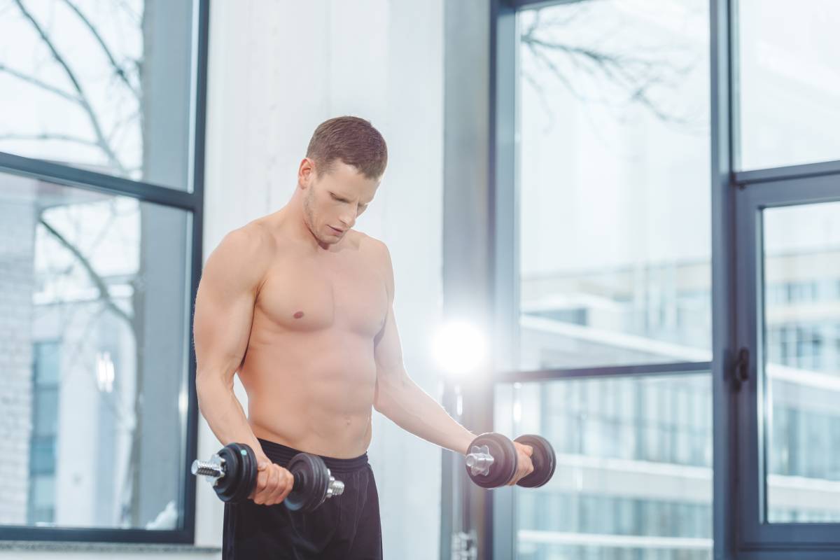 muscular shirtless sportsman exercising with dumbbells in gym